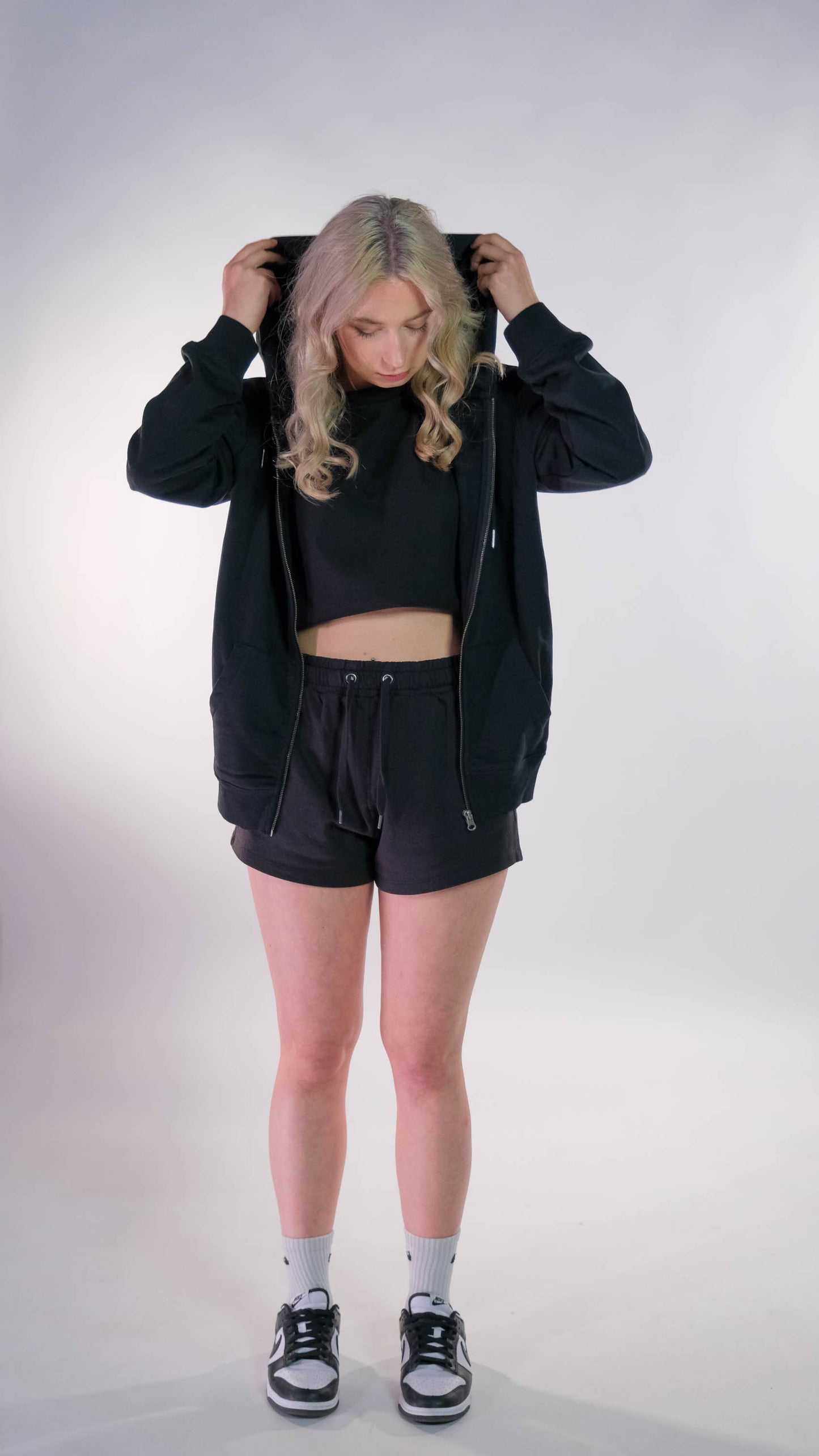 Vrouwelijk model met zwart, open gedragen, vest met wit 'FØØL' logo op de borst.