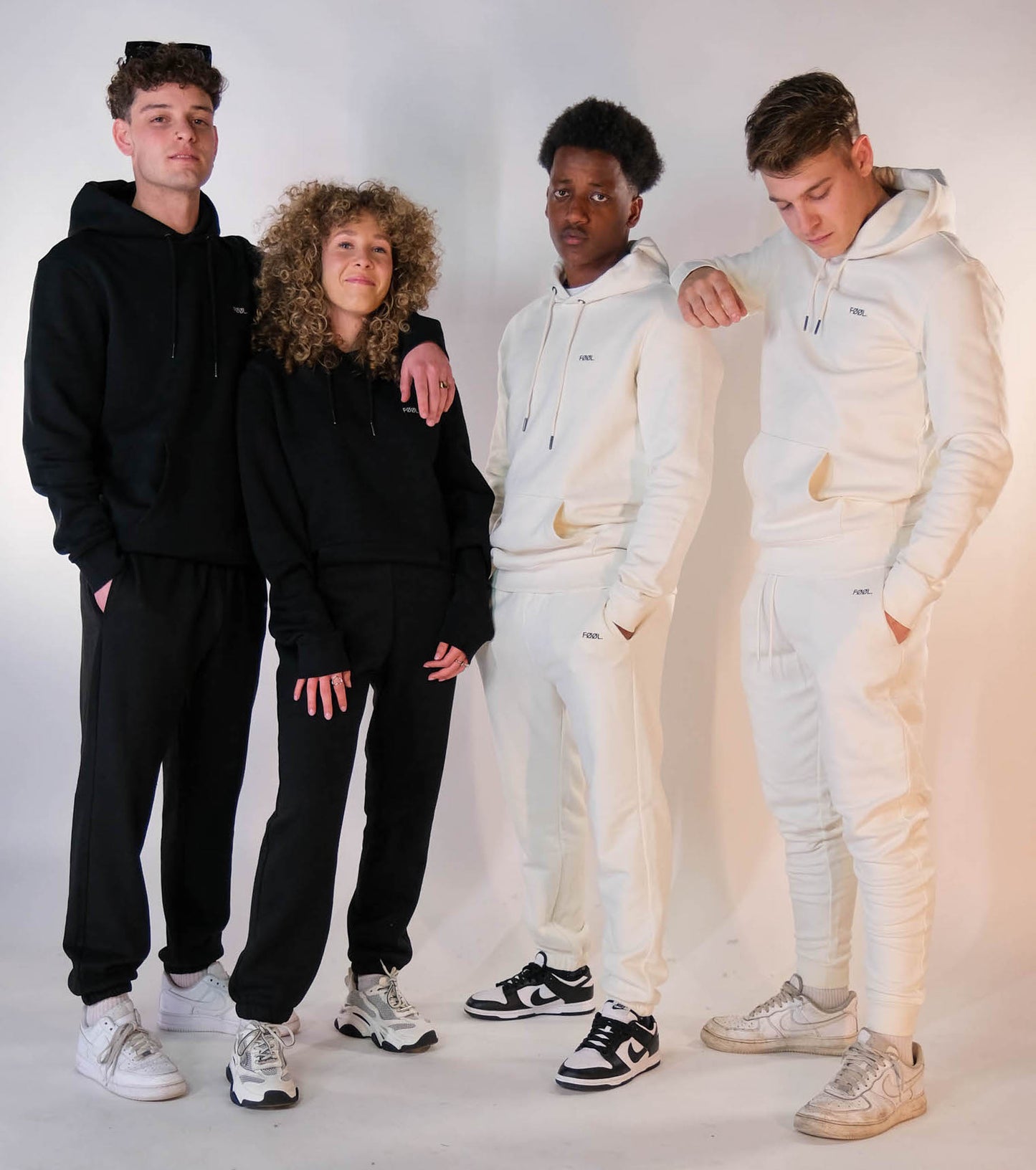 4 modellen die de 'FØØL' hoodie met bijpassende jogger dragen. 2 dragen de zwarte variant, 2 dragen de witte variant.