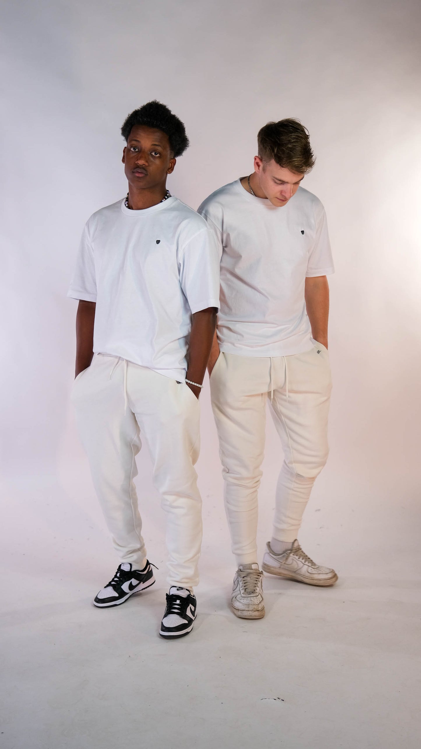 2 mannelijke modellen met een wit t-shirt met daarop een wit 'BEAR' logo. Beide modellen dragen ook een witte 'FØØL' joggers.