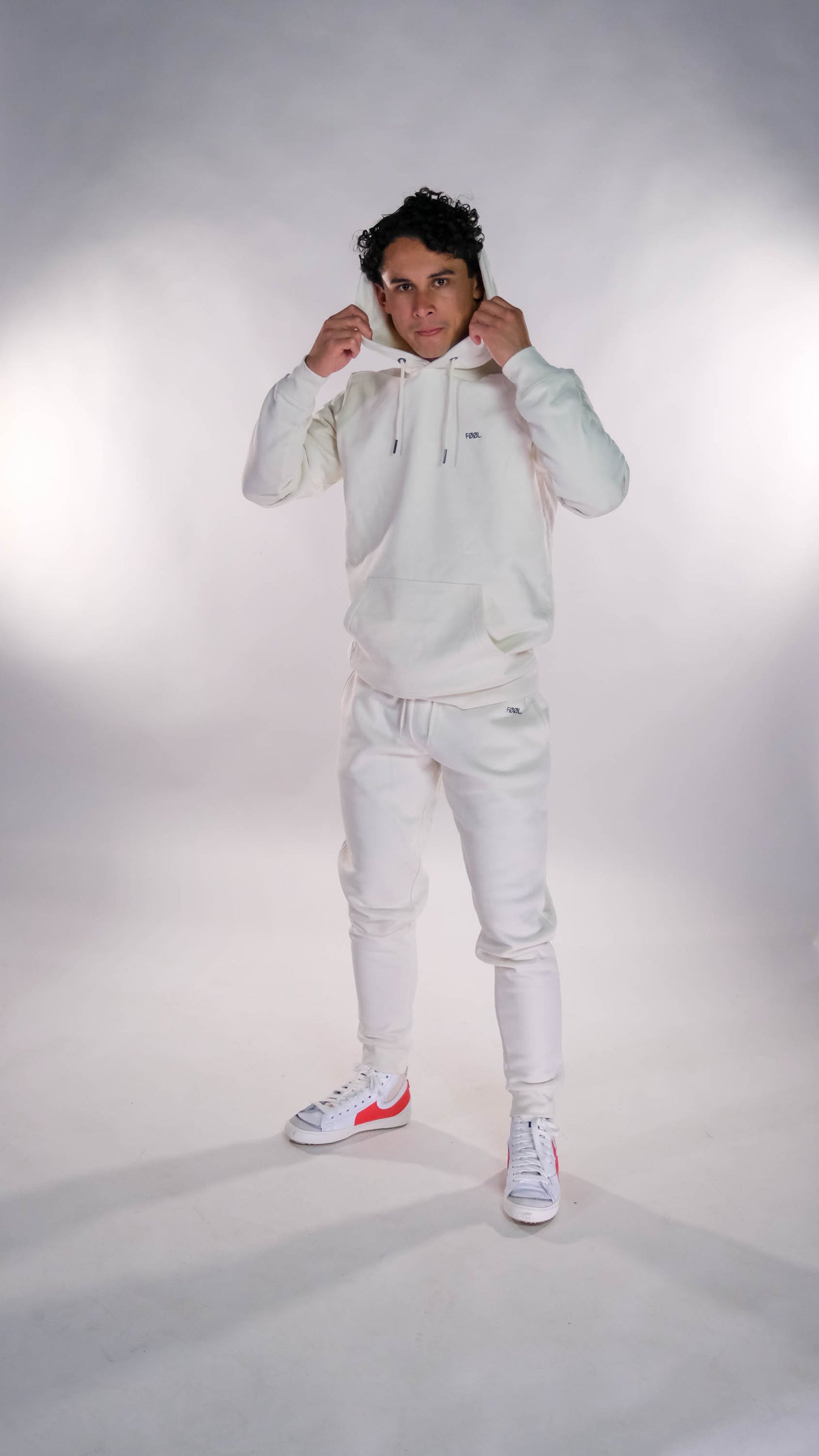 Mannelijk model met ivory hoodie en jogger, beide met zwart 'FØØL' logo.