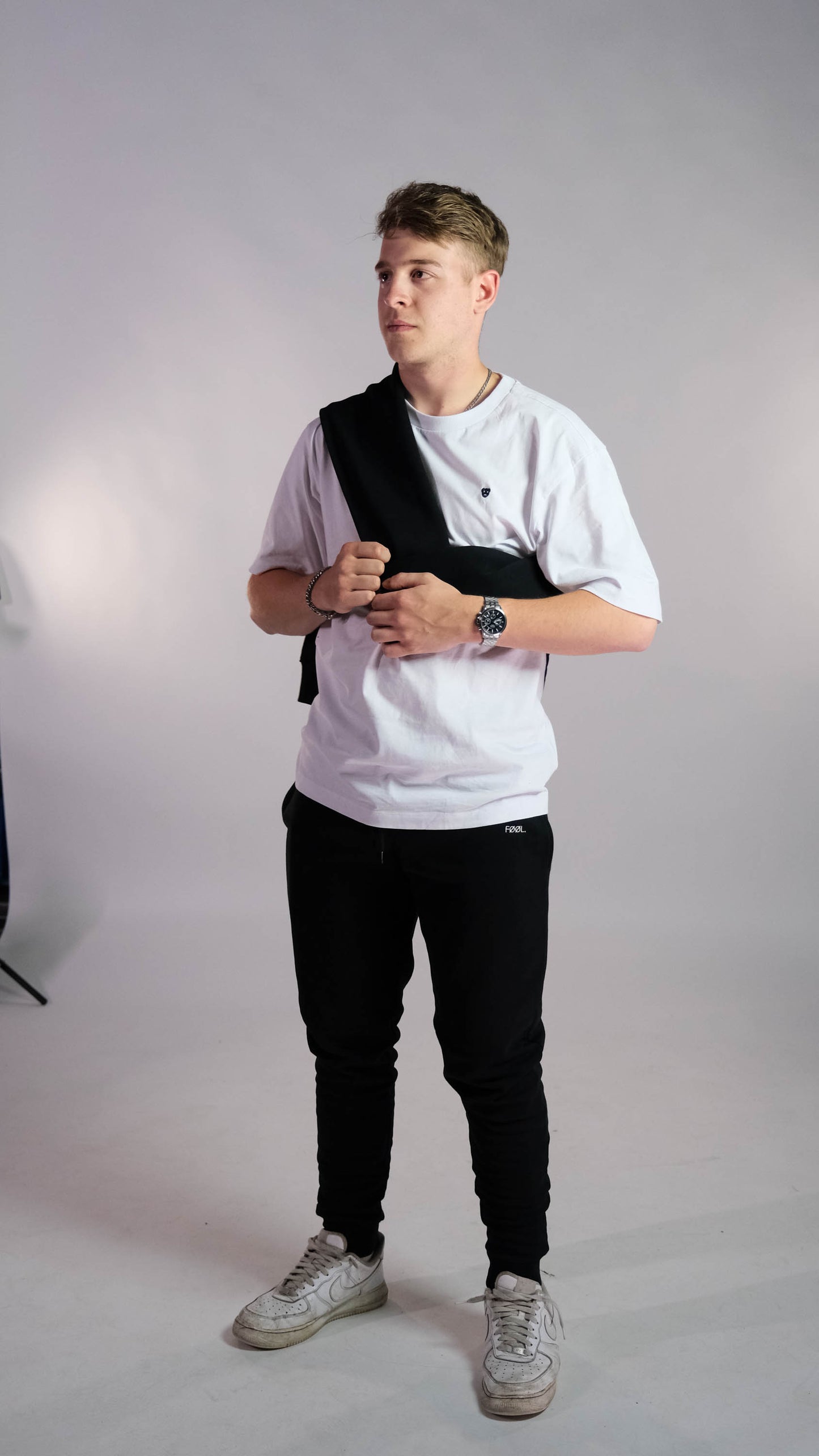 Mannelijk model met wit t-shirt met zwart 'BEAR' logo op de borst. Model draagt de zwarte jogger met het witte 'FØØL' logo.