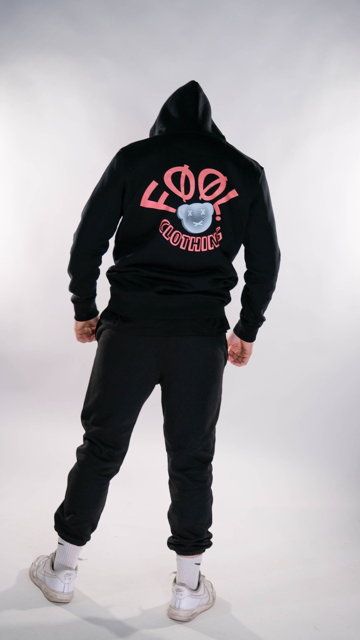 Jongen in zwarte hoodie en jogger met rood 'FØØL CLOTHING' logo op de achterkant