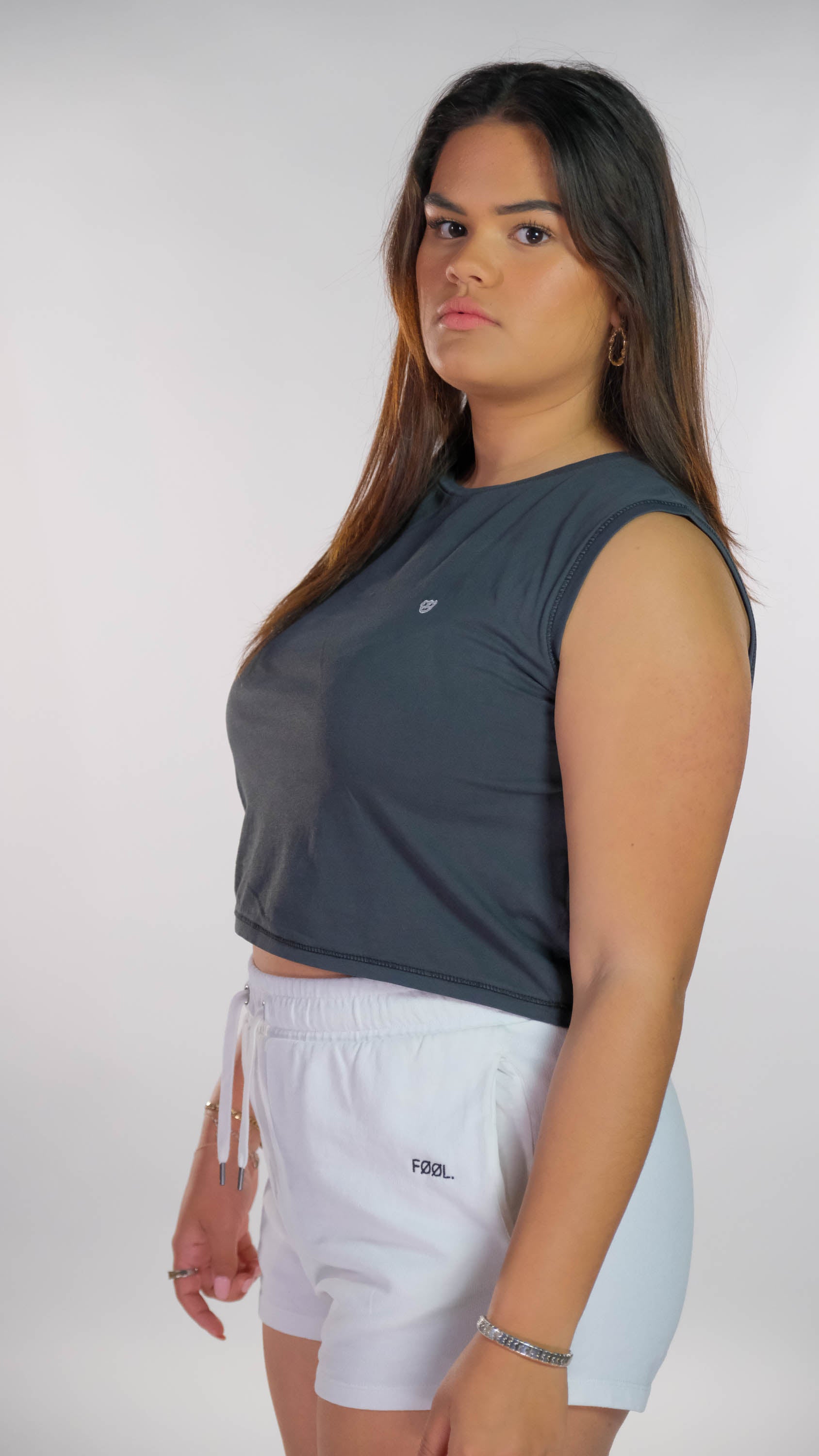 Vrouwelijk model draagt de verwassen zwarte cropped top met de witte 'BEAR' logo op de borst en een witte short met het zwarte 'FØØL' logo aan de zijkant.
