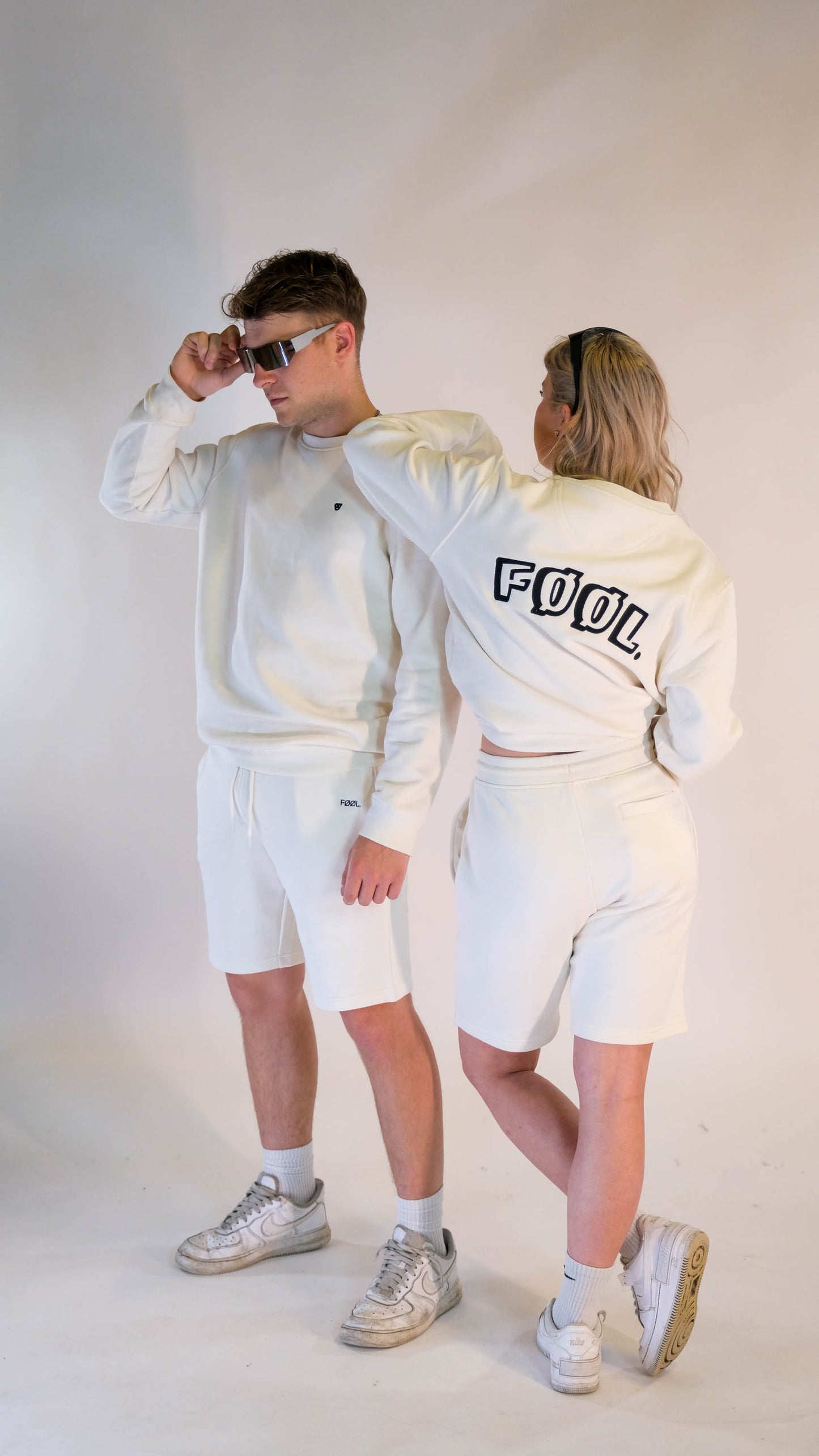 2 modellen. Een mannelijk model met de ivory 'FØØL' sweater met het zwarte 'BEAR' logo op de borst en draagt daarbij de ivory 'FØØL' short. Het vrouwelijke model draagt hetzelfde maar staat met haar rug naar de camera toe.