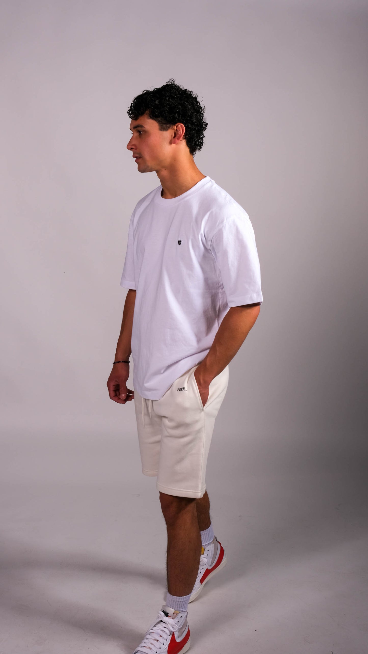 Mannelijk model met wit t-shirt met daarop het zwarte 'BEAR' logo. Ook draagt hij de ivory shorts.