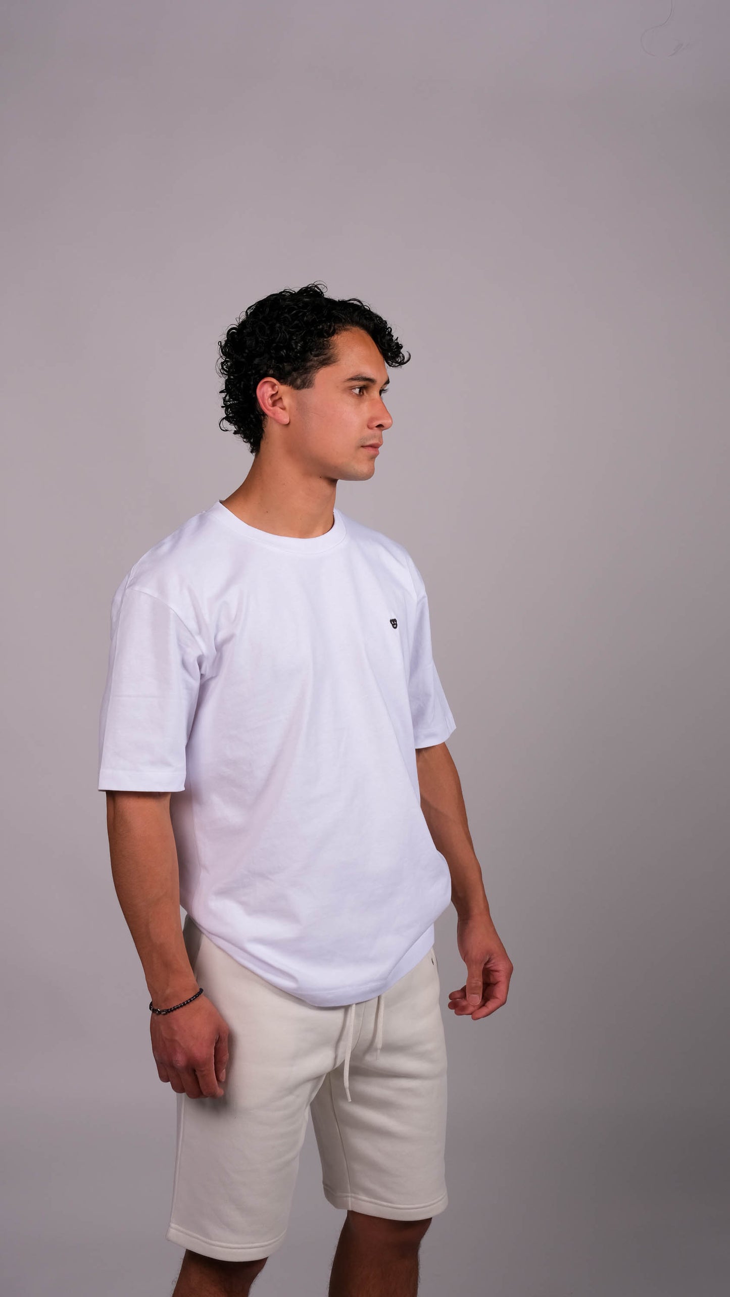 Mannelijk model met wit t-shirt met daarop het zwarte 'BEAR' logo. Ook draagt hij de ivory shorts.