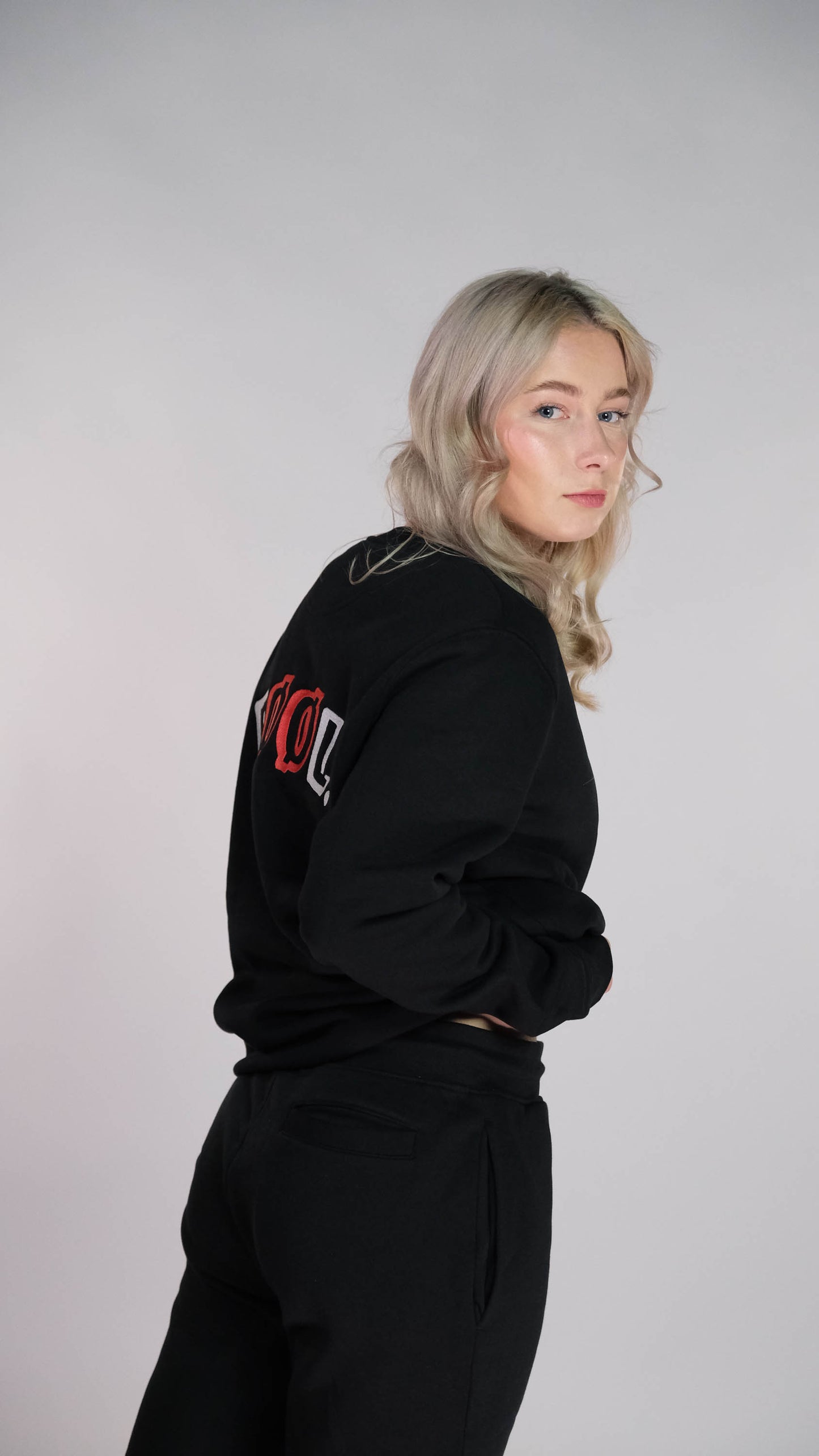 Vrouwelijk model met de zwarte sweater met het 'FØØL' logo op haar rug. Ook draagt zijn de zwarte 'FØØL' short.