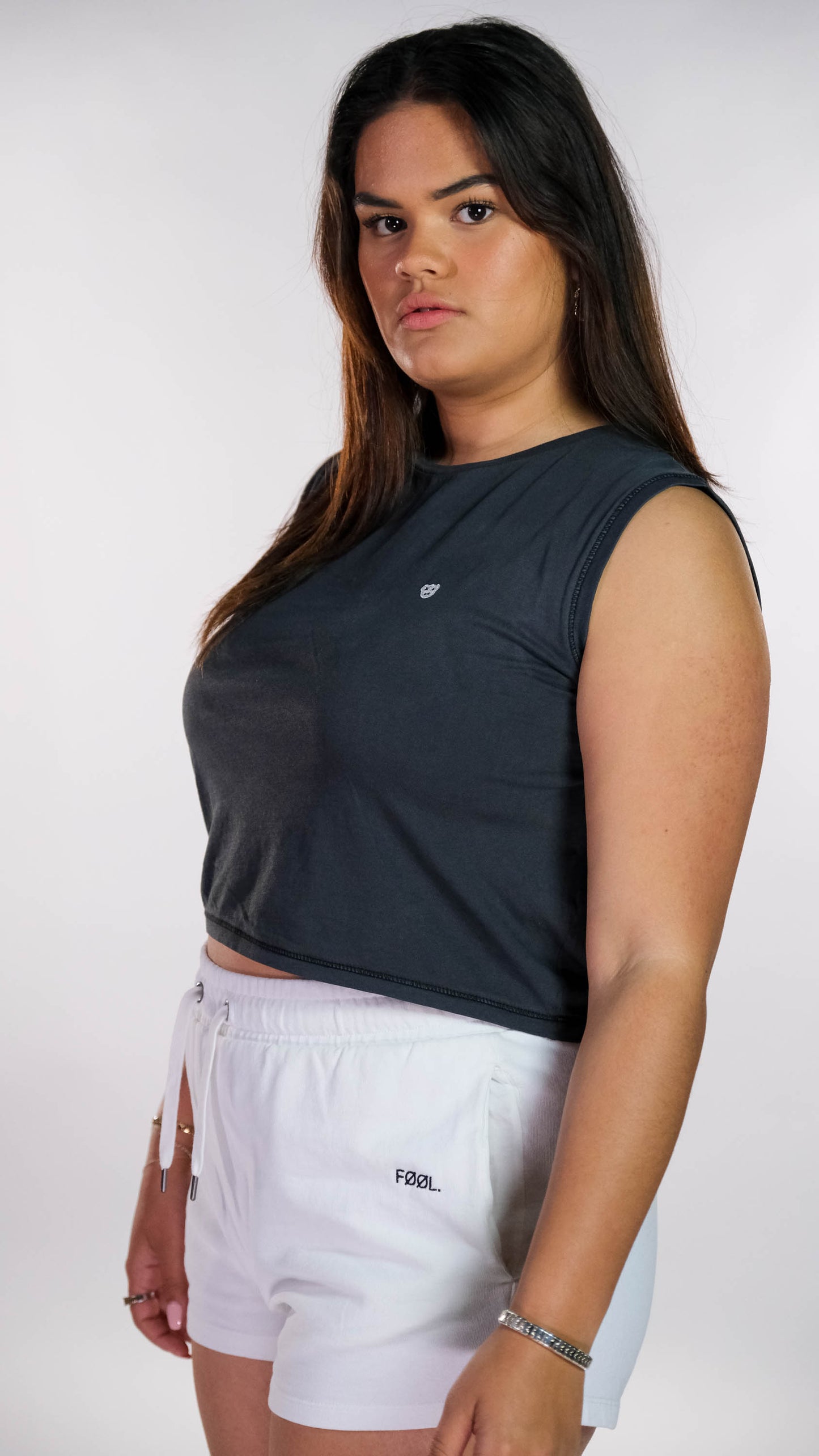 Vrouwelijk model draagt de verwassen zwarte cropped top met de witte 'BEAR' logo op de borst en een witte short met het zwarte 'FØØL' logo aan de zijkant.