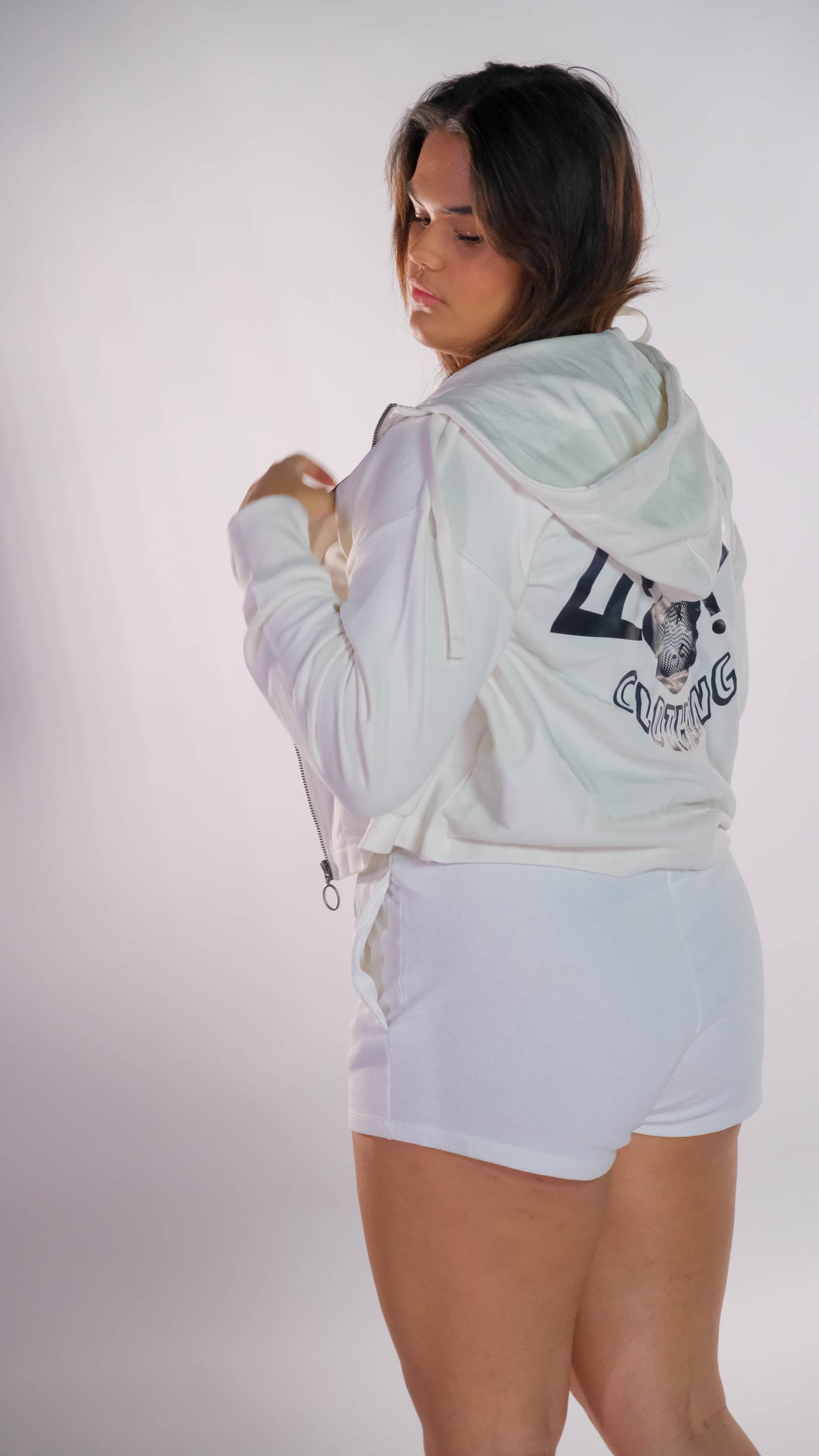 Vrouwelijk model die half met haar rug naar de camera is gedraaid. Zij draagt de oversized cropped vest in de kleur ivory met het zwarte 'FØØL CLOTHING' logo op de rug. Ook draagt zij de ivory dames short.