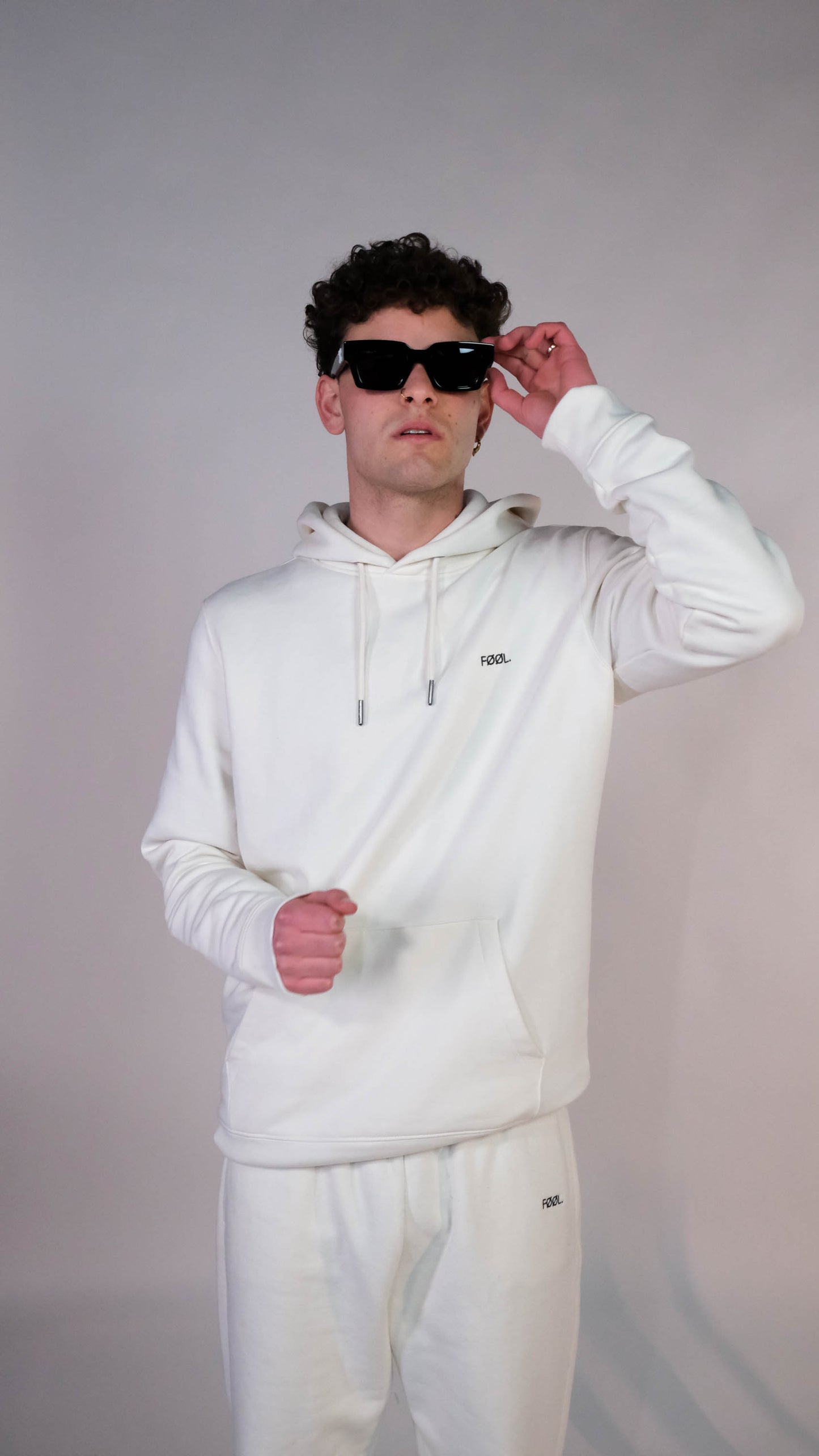 Mannelijk model met de ivory sweater met het zwarte 'FØØL' logo op de borst. Ook draagt hij een zonnebril en de ivory jogger met het zwarte 'FØØL' logo.